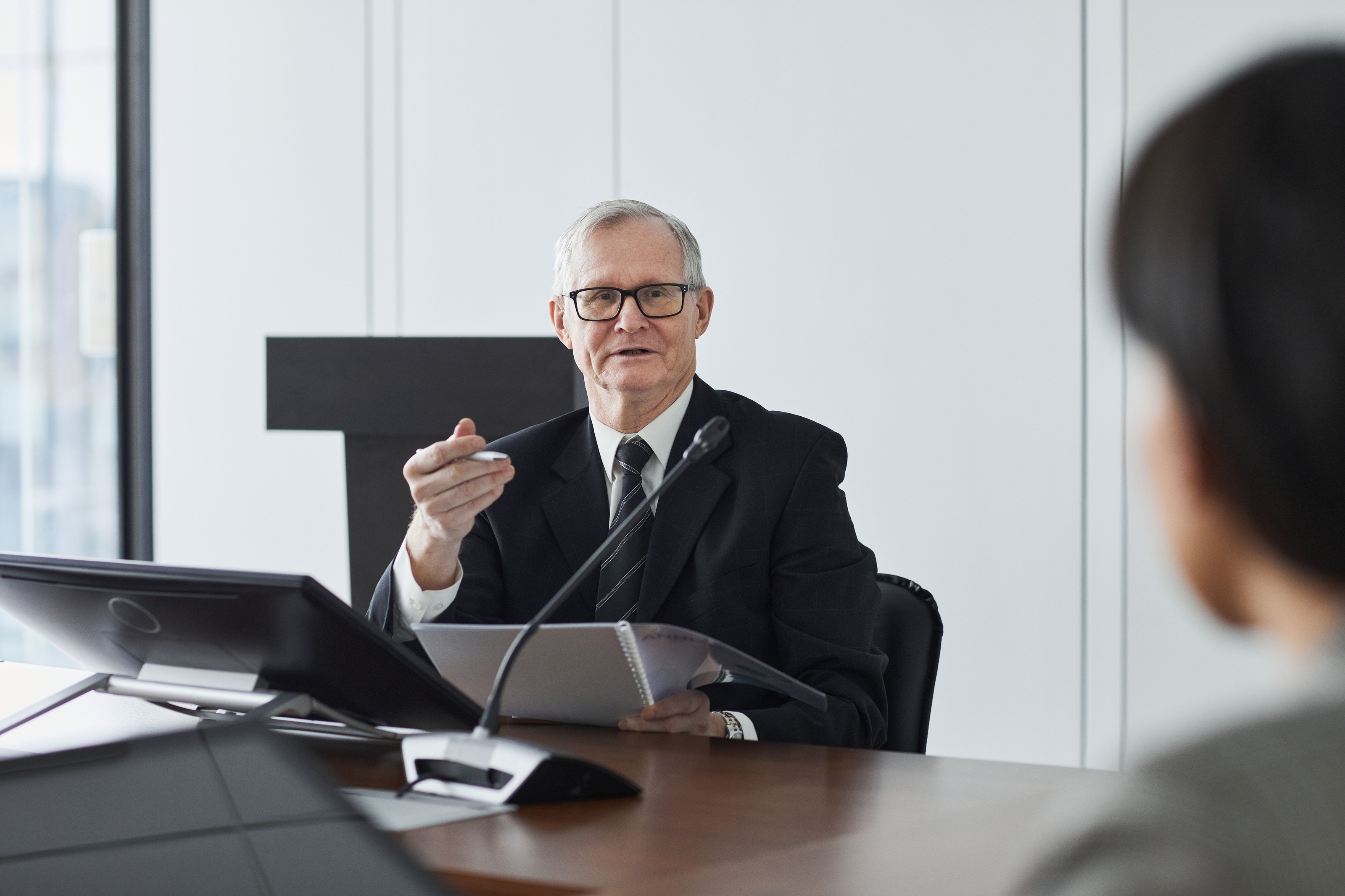 Licensed stock photograph of a gray-haired senior executive in a dark suit speaking at a boardroom table in a high-rise office, not Insight Funders staff